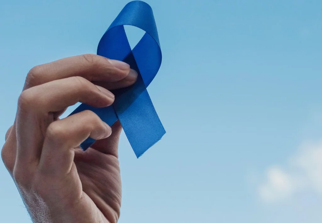A hand holding a blue ribbon in the air representing mental health